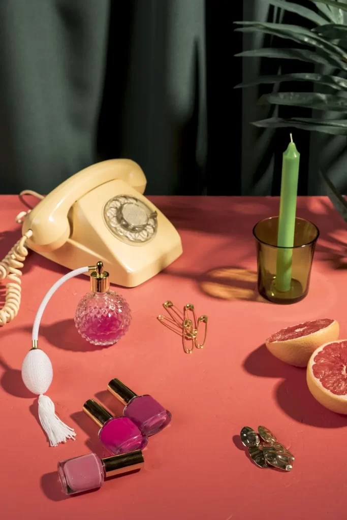 High-angle composition with vintage phone, perfume, nail polish and grapefruit on a colourful table.
