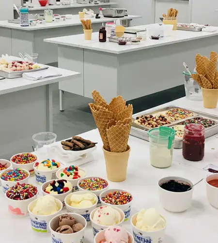 Colorful toppings, cones, and ice cream scoops set up on tables for a creative cooking workshop for kids focused on ice cream making in Dubai