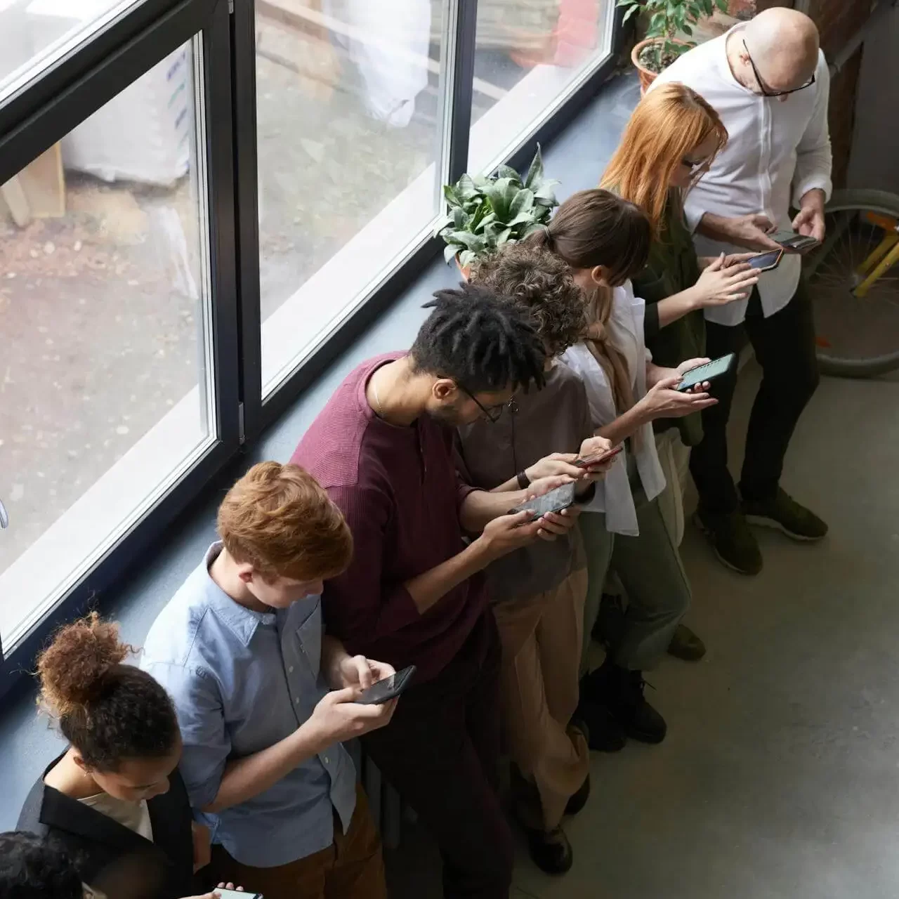 Group of people chatting and using smartphones near floor-to-ceiling windows at a product launch event organised by MRM Events.