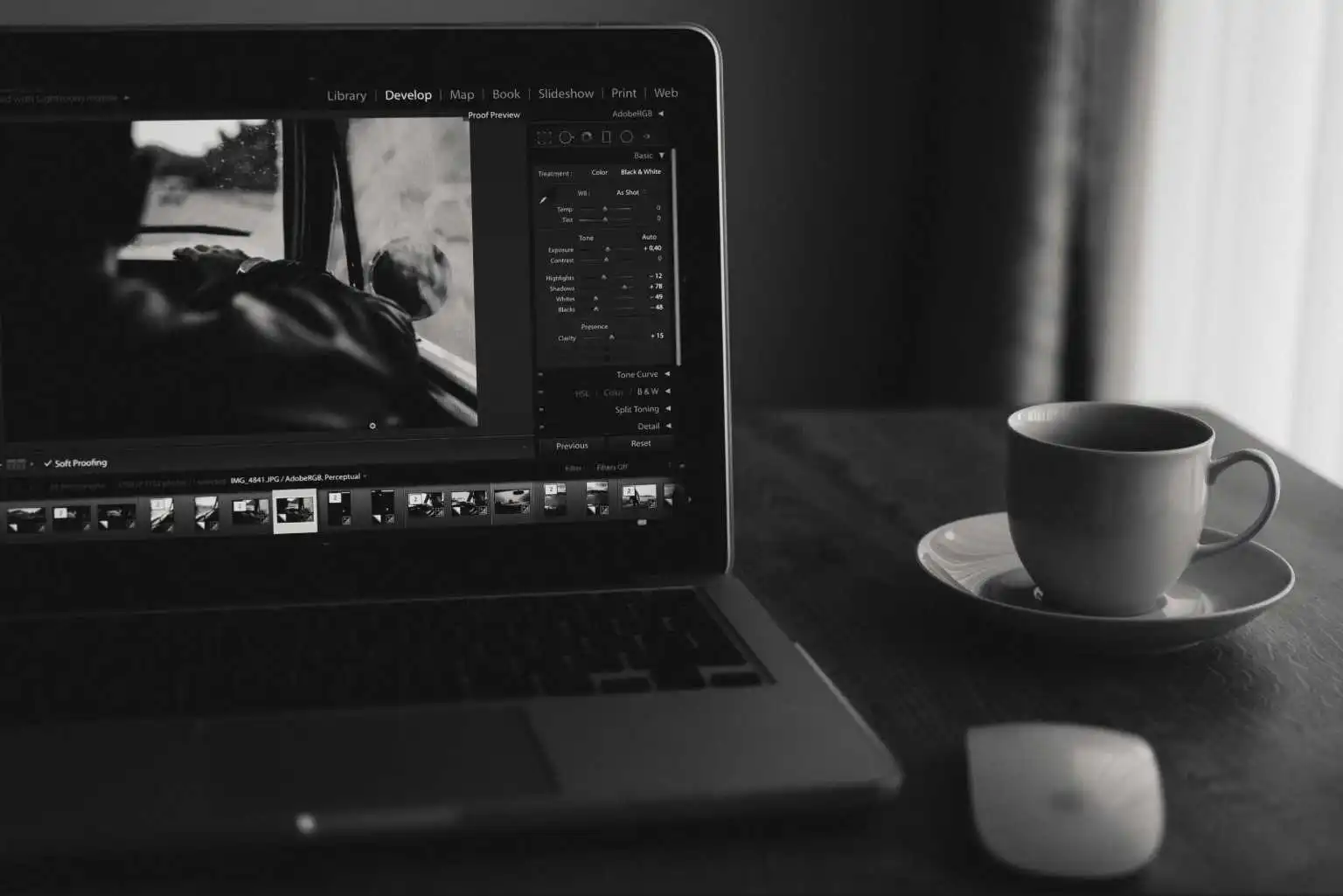 Black and white close-up of a laptop running photo-editing software with a coffee cup and mouse, representing MRM Events creative workspace.