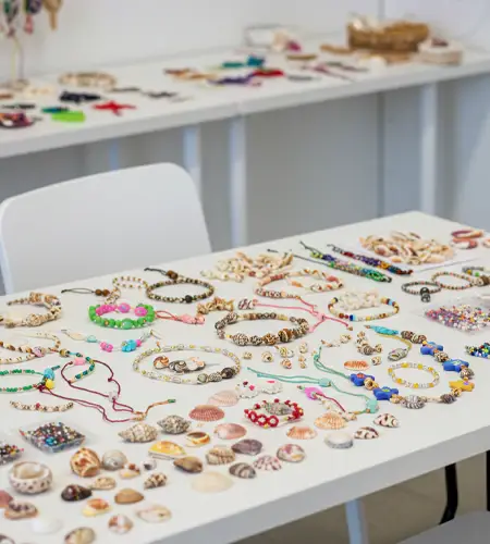 Shell jewelry making workshop setup for kids in Dubai, featuring handmade necklaces, bracelets, and seashell crafts displayed on white tables in a bright classroom setting