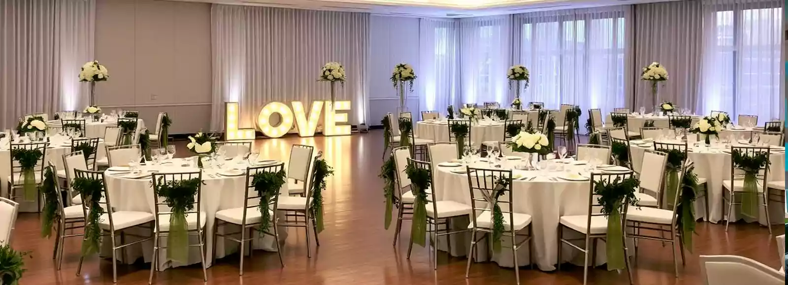 Elegant indoor arabic wedding reception setup in Dubai with round tables, floral centerpieces, and illuminated 'LOVE' sign as decor.