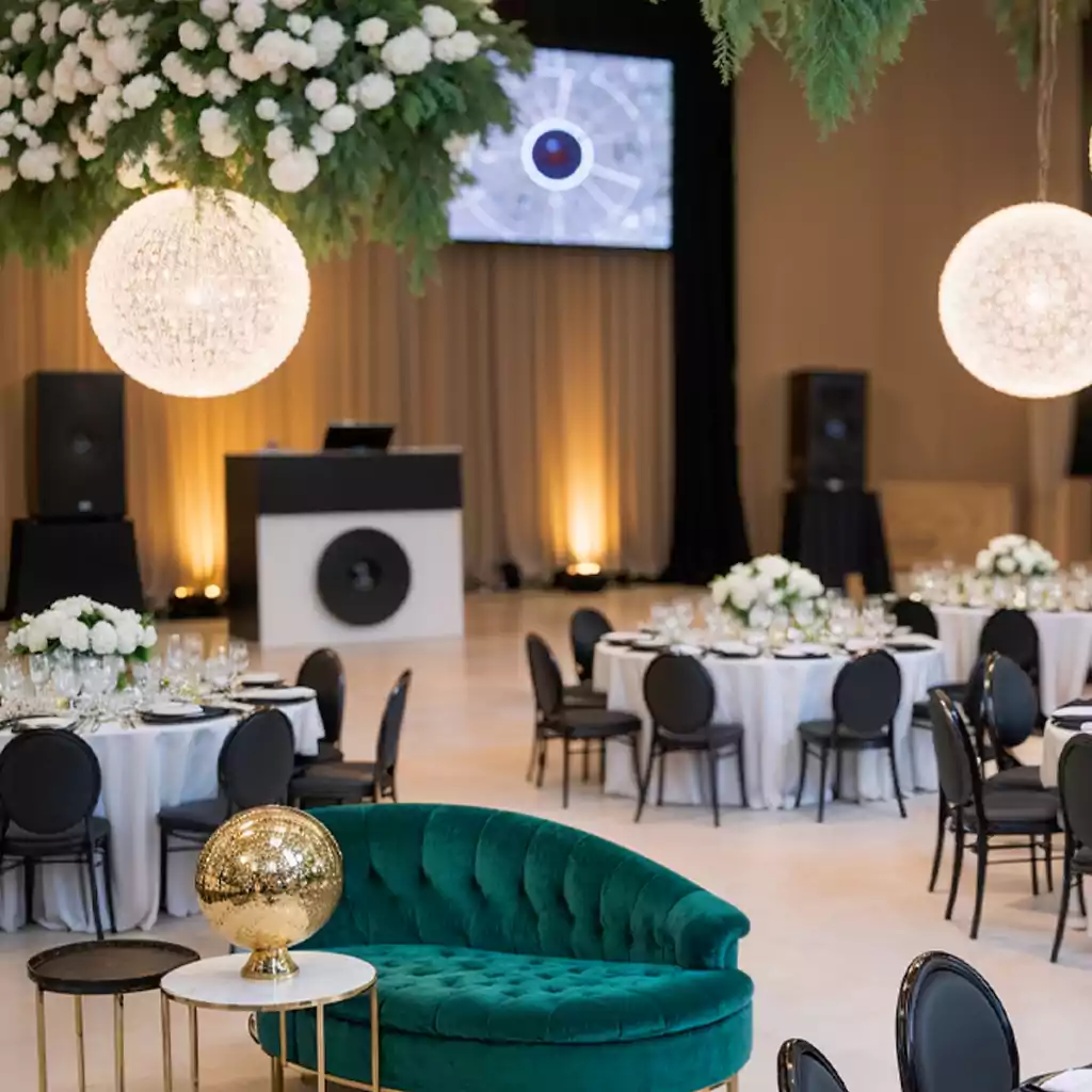 Luxurious wedding reception setup featuring a plush emerald green sofa, black and white round tables with elegant floral centerpieces