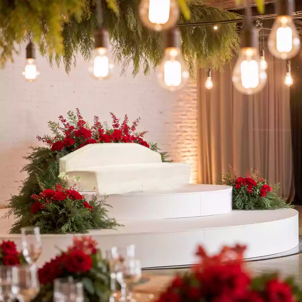 Elegant wedding stage with white seating, red floral arrangements, and warm hanging lights.